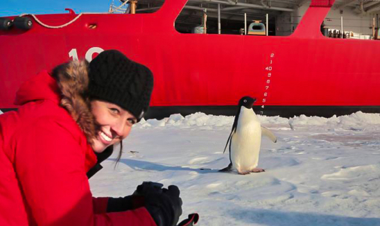 Woman in the arctic in the foreground with a penguin in the background