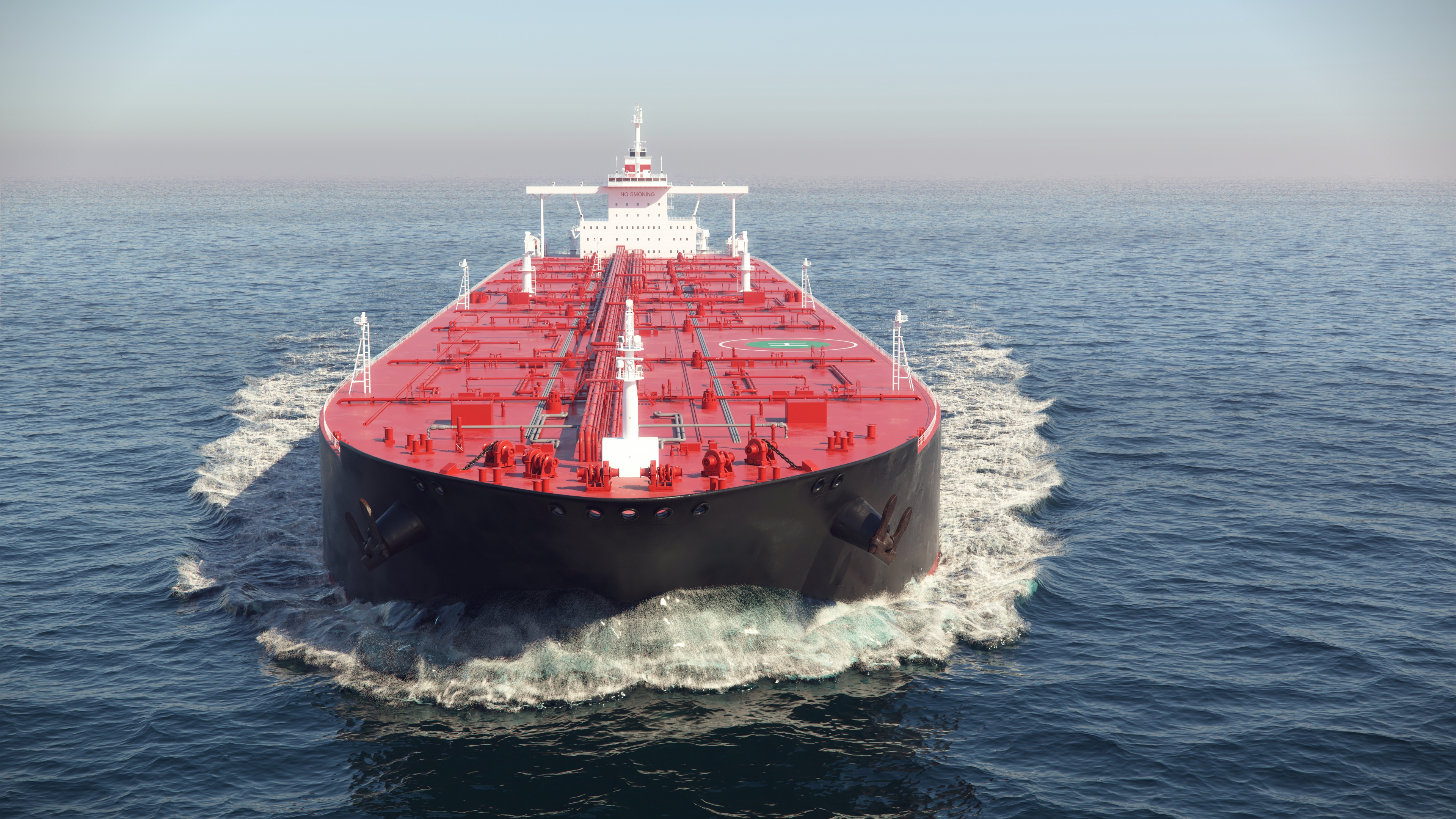 A front-facing view of a massive commercial oil tanker with a black hull and a red deck covered in intricate piping, sailing forward through the open ocean.
