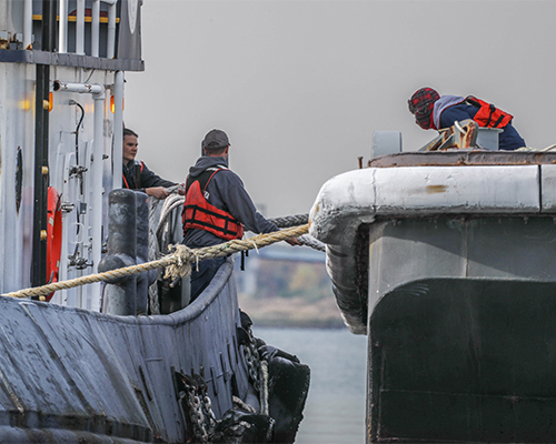 Three people wearing orange safety vests tying a rope between a boat and dock.